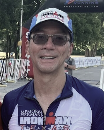 Ron Tran smiling and wearing sunglasses, a baseball cap and shirt reading "Iron Man".